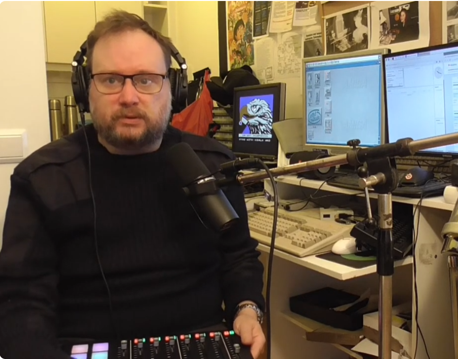 A picture of DJ Daemon in front of some Commodore computers in 2020.